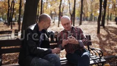一位<strong>年迈</strong>父亲的成年儿子在秋公园的长凳上教智能手机。